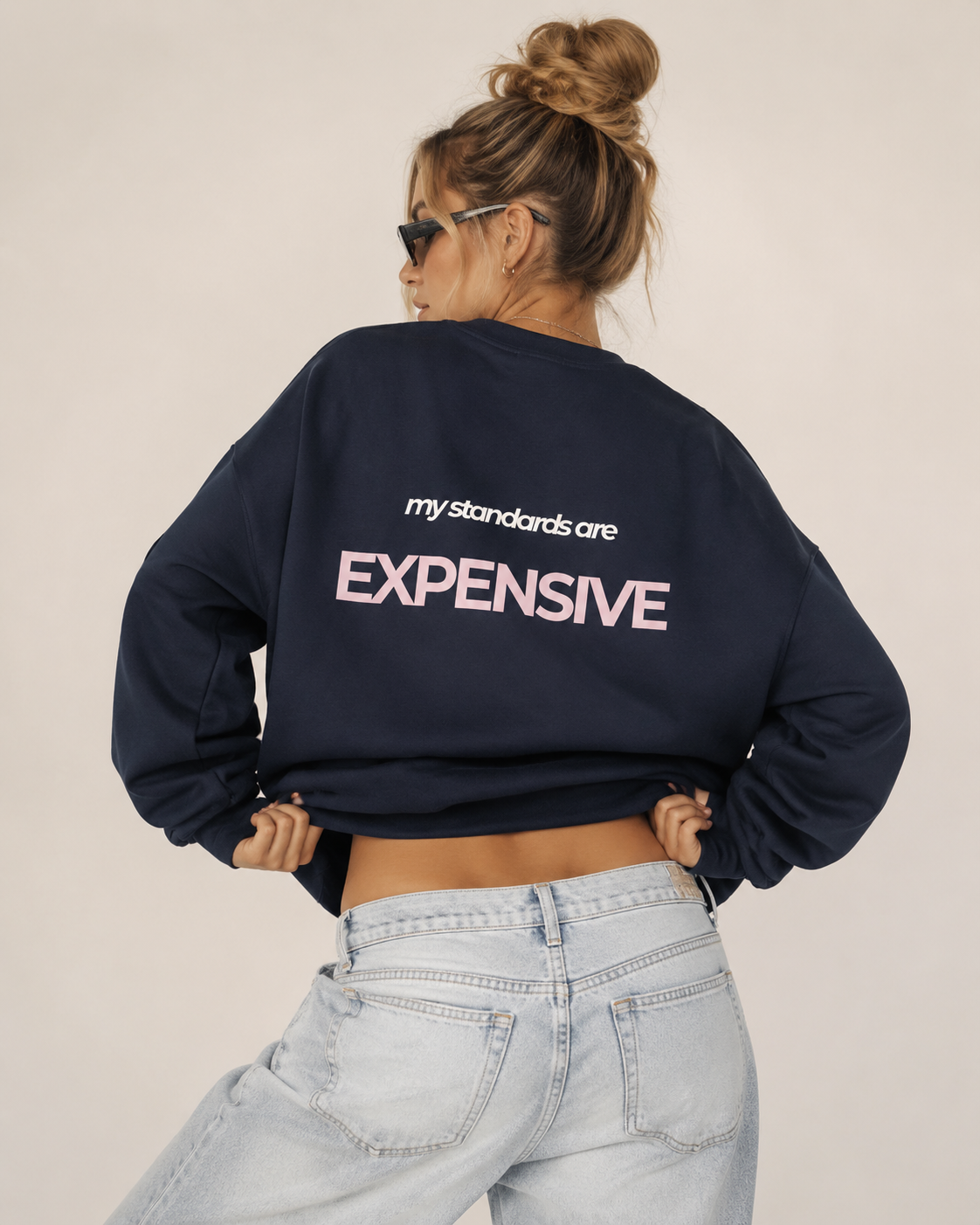 Woman wearing an oversized navy crewneck sweatshirt with a pink and white My Standards Are Expensive back print