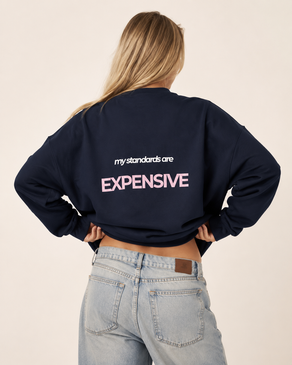 Woman wearing an oversized navy crewneck sweatshirt with a pink and white My Standards Are Expensive back print

