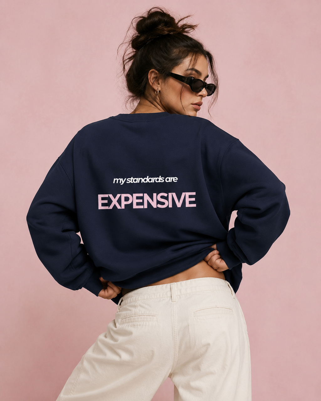 Woman wearing an oversized navy crewneck sweatshirt with a pink and white My Standards Are Expensive back print
