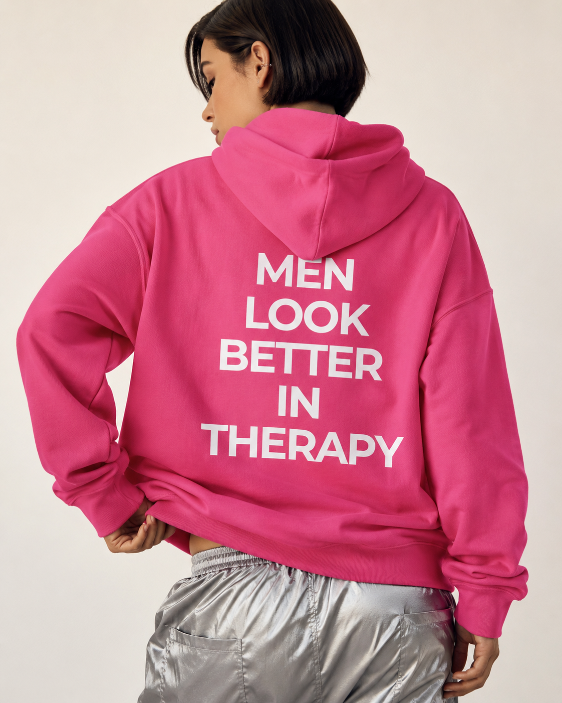 Bright pink unisex hoodie with a white “Men Look Better in Therapy” statement print across the back.
