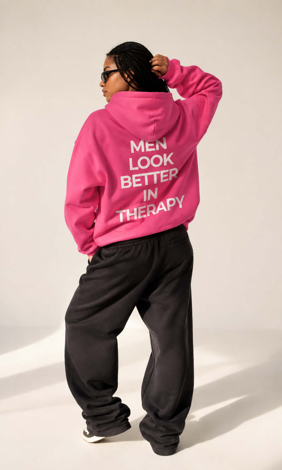 Bright pink unisex hoodie with a white “Men Look Better in Therapy” statement print across the back.
