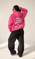 Bright pink unisex hoodie with a white “Men Look Better in Therapy” statement print across the back.
