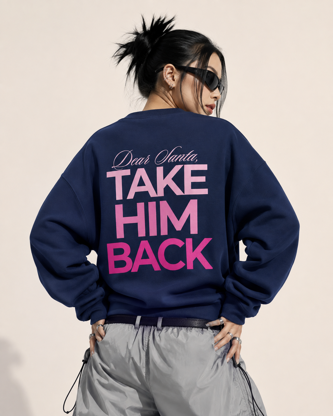 Model wearing a navy Dear Santa Take Him Back sweatshirt with pink back print and silver cargo pants
