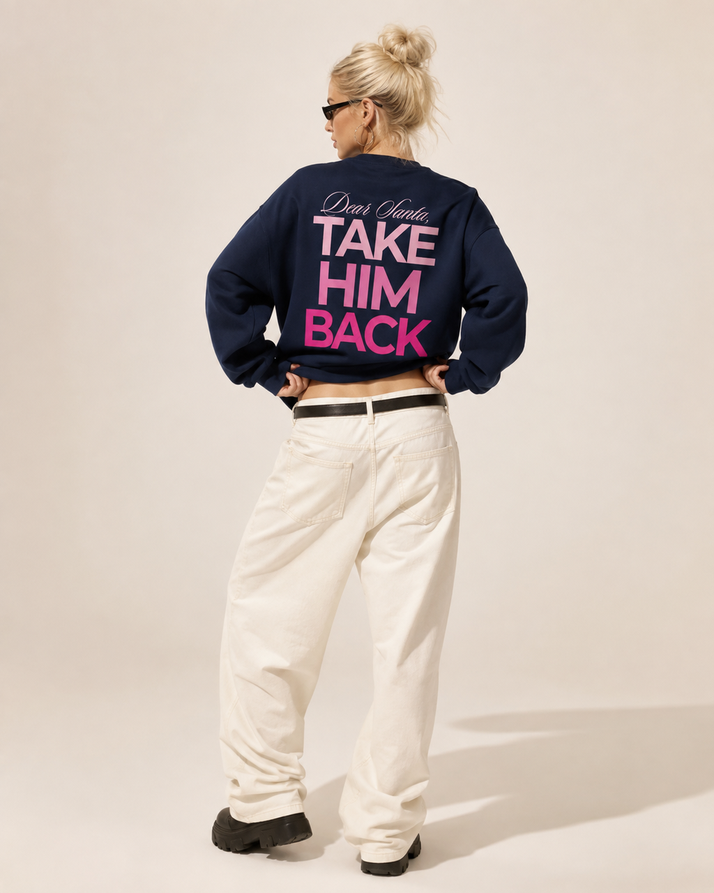Back view of a navy Dear Santa Take Him Back graphic sweatshirt styled with white trousers