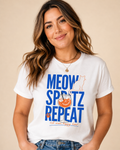Woman wearing a white organic cotton Meow Spritz Repeat cat mom T shirt with blue and orange graphic print.