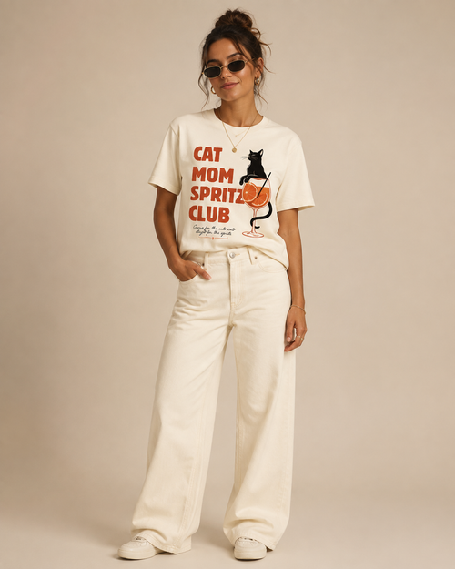 Woman wearing a cream organic cotton Cat Mom Spritz Club T shirt with a colourful cat and spritz glass graphic.