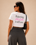 Woman wearing a white feminist crop top with the slogan “Rejecting men is self care” in black and pink typography.