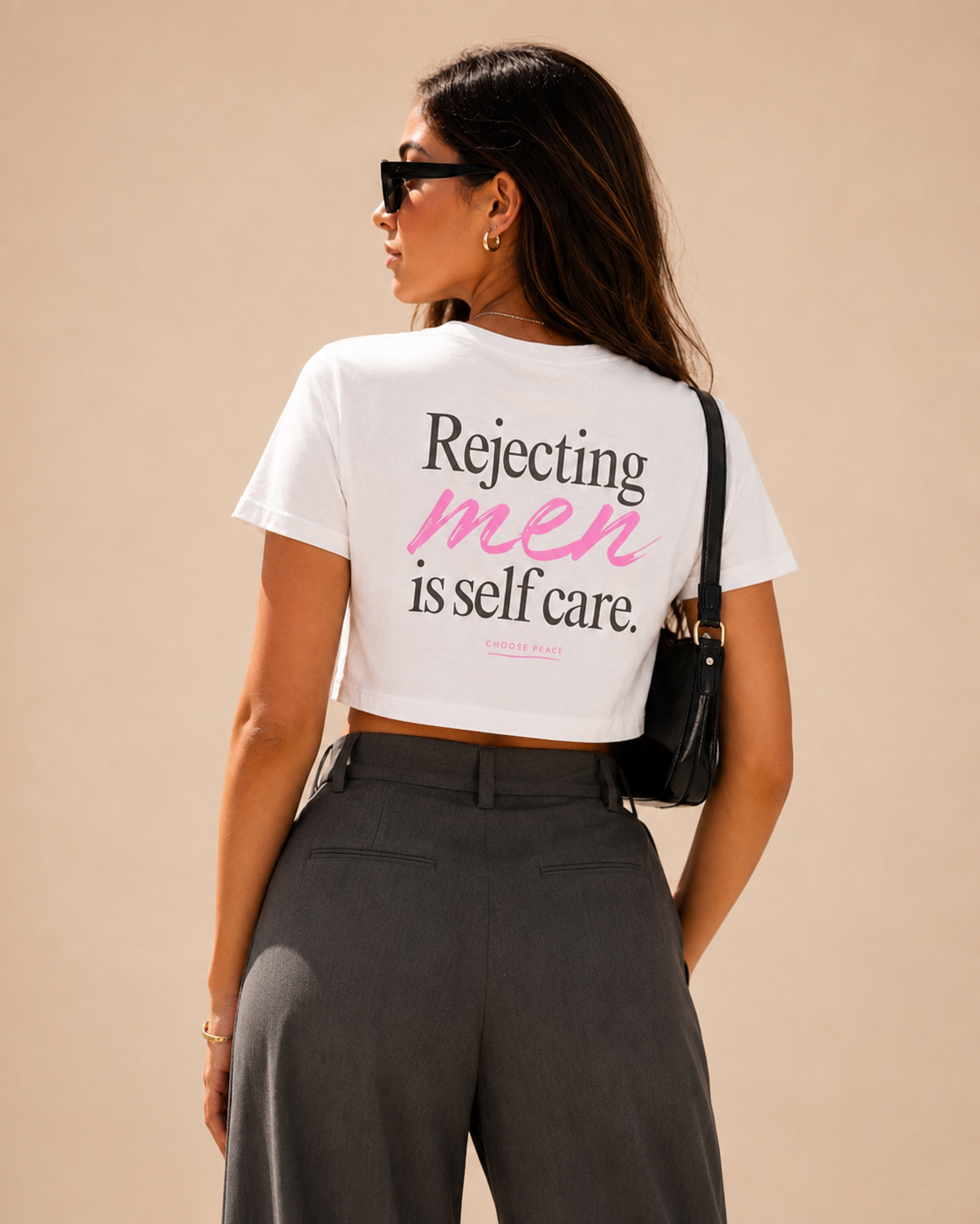 Woman wearing a white feminist crop top with the slogan “Rejecting men is self care” in black and pink typography.